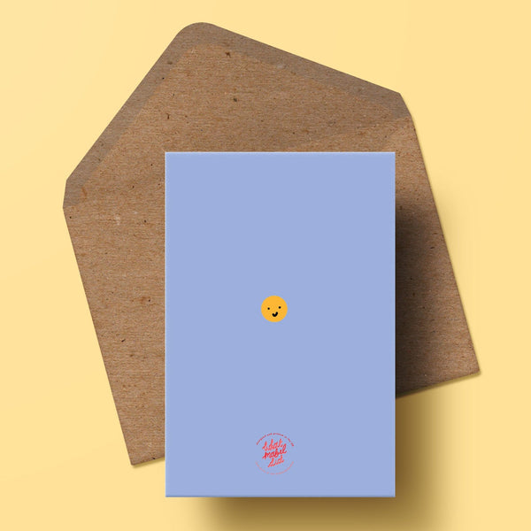 an image showing the back of the greetings card with whatmabeldid logo and a small central smiley face. the colour of the background is the same blue as the front of the card. there is a recycled kraft envelope shown behind the card.