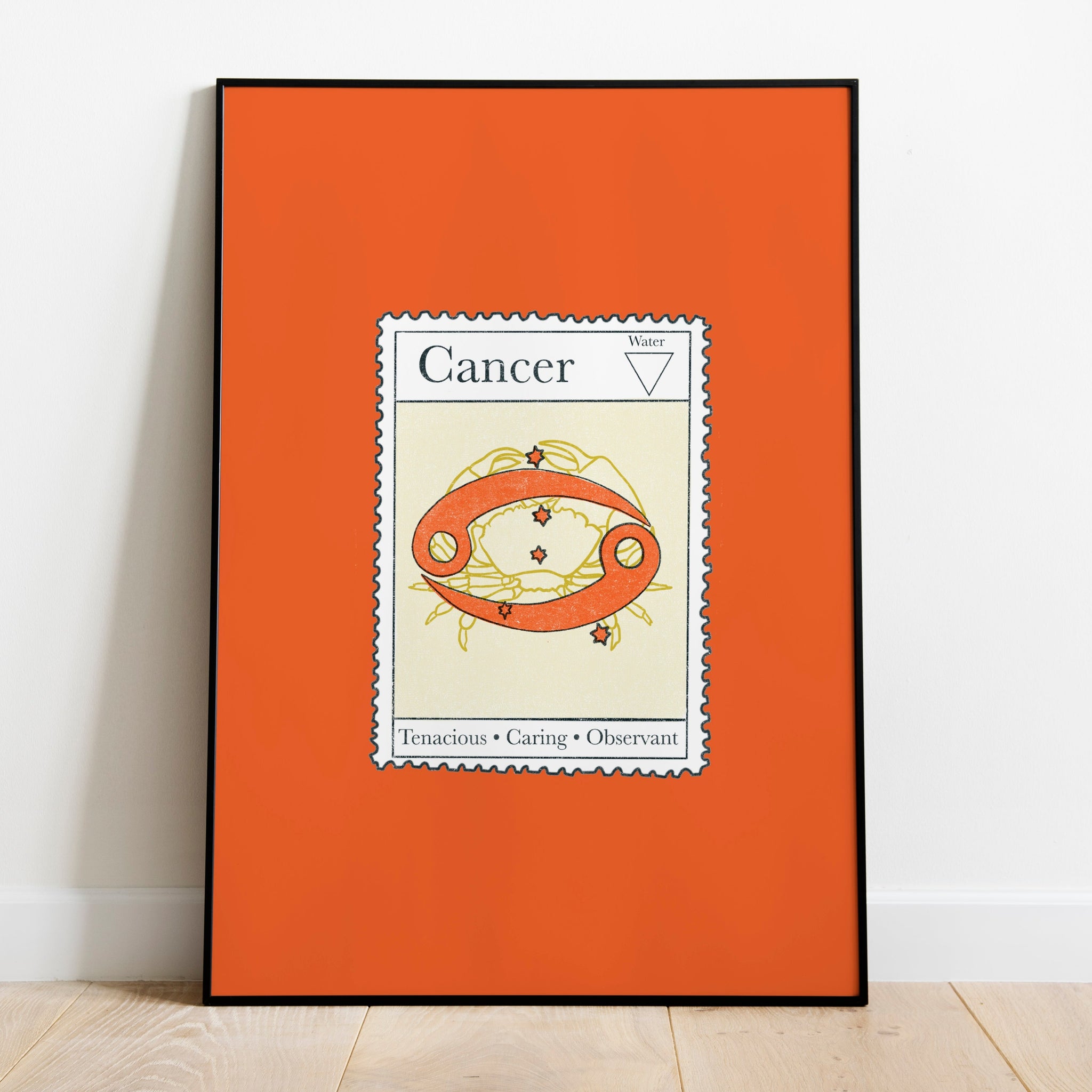 Image of a framed art print leaning against the wall. The art print itself is a postage stamp representing the star sign of cancer. The print is bright and colourful in shades of green, cream and tomato red.