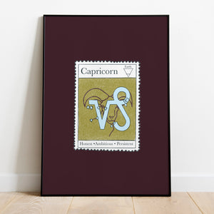 Image of a framed art print leaning against the wall. The art print itself is a postage stamp representing the star sign of Capricorn. The print is bright and colourful in shades of maroon, sage and baby blue.
