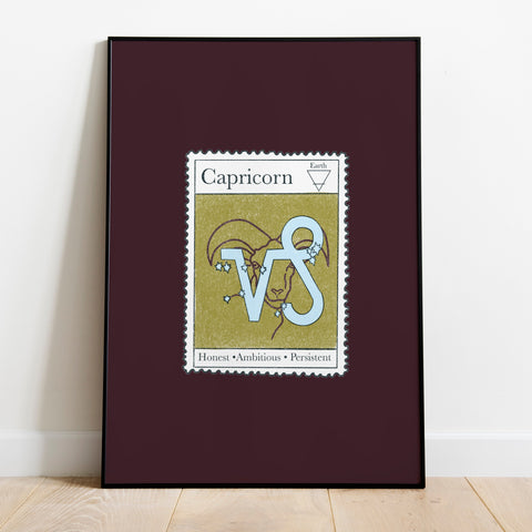 Image of a framed art print leaning against the wall. The art print itself is a postage stamp representing the star sign of Capricorn. The print is bright and colourful in shades of maroon, sage and baby blue.