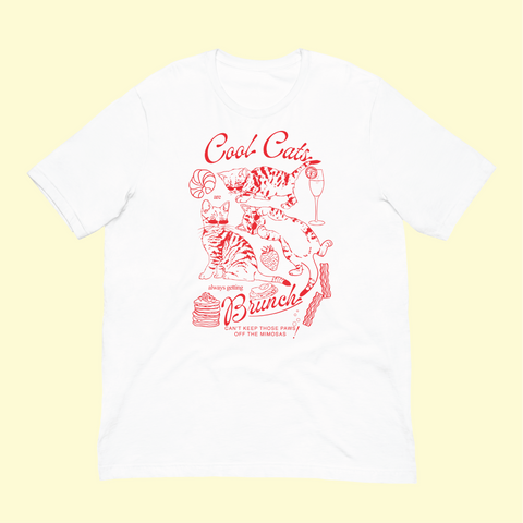 image of a white t shirt with a graphic on it depicting three kitten in red line art alongside brunch foods. The text around them reads 'cool cats are always getting brunch' with 'can't keep those paws off the mimosas' beneath