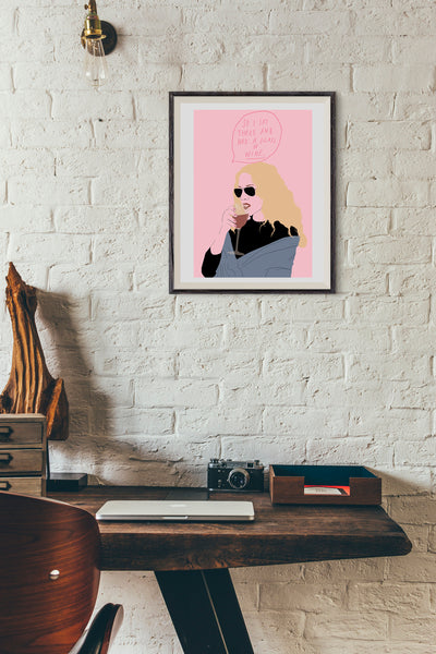 illustration of carrie bradshaw from sex and the city drinking a glass of wine. above her in a speech bubble is the phrase so i sat there and had a glass of wine. The background is a medium pink. the print is framed and in a home office type space.