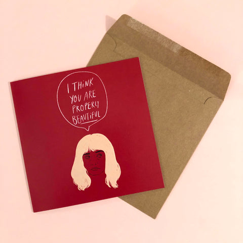 image of a square card featuring an illustration of alyssa from the end of the f***ing world with a speech bubble above her head saying 'I think you a properly beautiful'. the background of the card is a vibrant red, behind the card is a recycled kraft envelope