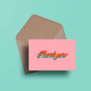 photograph of a pink landscape thank you card with the words thank you written in rainbow cursive. there is a matching brown kraft envelope behind it.