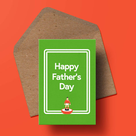 image of a green greetings card with a small subbuteo figure in the centre along with double white lines reminiscent of a football pitch along with the words 'happy father's day' behind the card is a recycled kraft envelope.