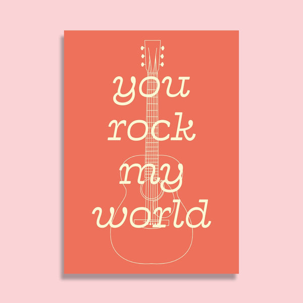 postcard featuring an illustration of an acoustic guitar with the words you rock my world overlaid, both the drawing and text are in a cream colour. the background is a pale coral red.