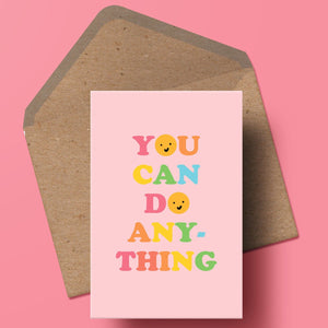 image of a greetings card featuring the words you can do anything in a bold 70s type with alternating rainbow colours for each letter. the Os have been replaced with smiley faces and the background of the card is a pale pink. the card is sat on top of a kraft envelope.