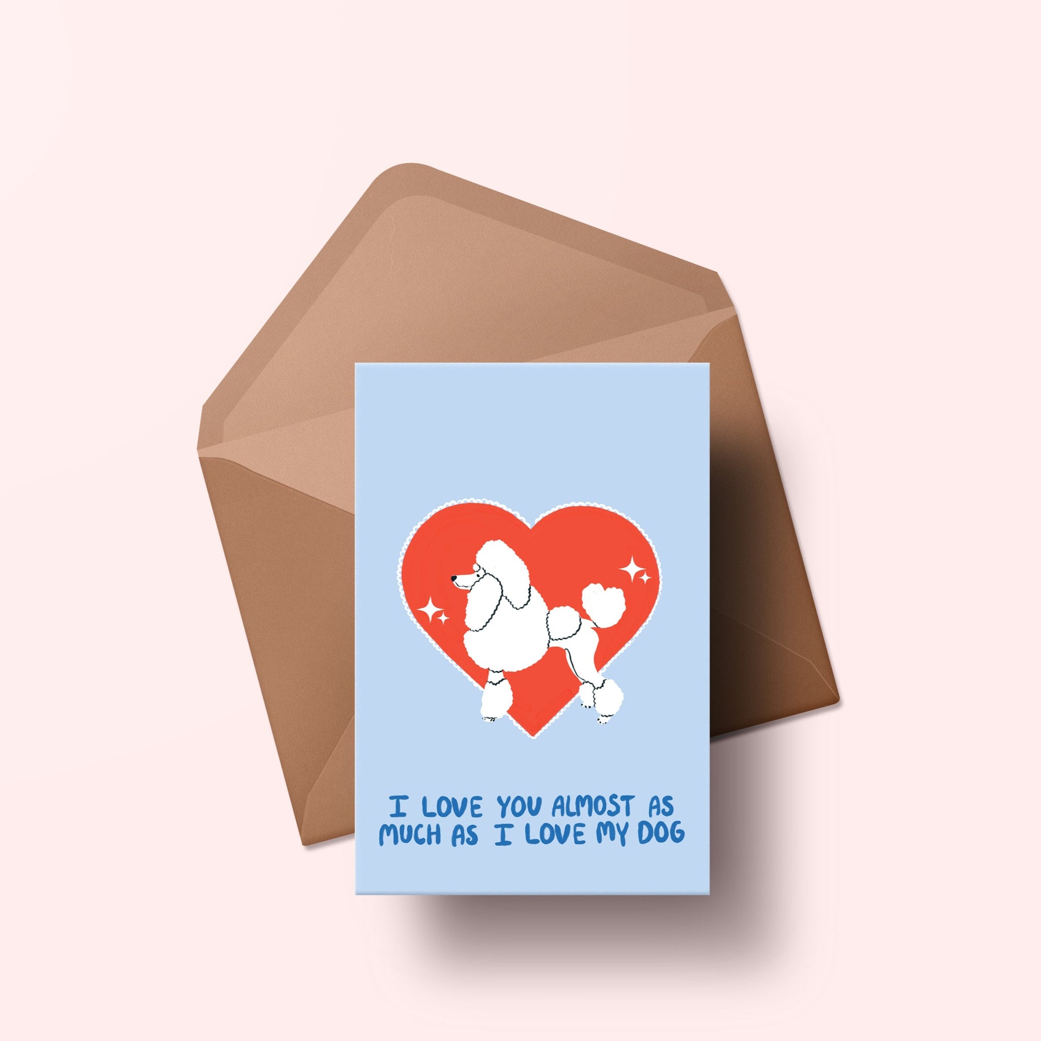image of a greetings card featuring an illustration of a poodle with a red heart behind it. The background of the card is a light blue and beneath the heart and dog are the words I love you almost as much as my dog in handwritten lettering in a darker blue shade. Behind the card is an envelope made of a recycled kraft material.
